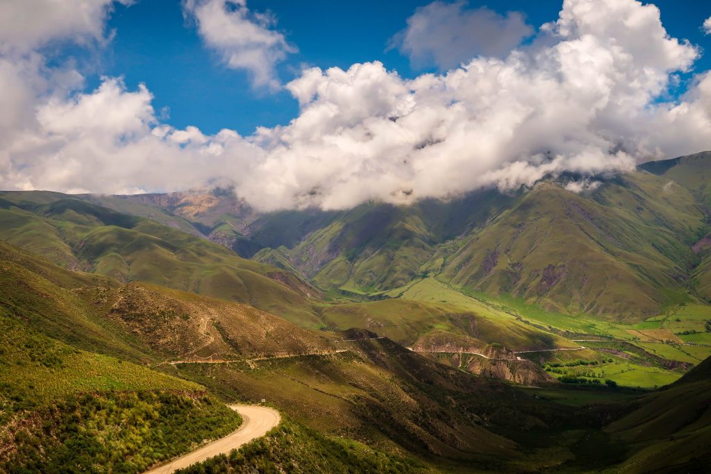 A landscape view of a dirt road going through the green hills and mountains of Salta, Argentina.