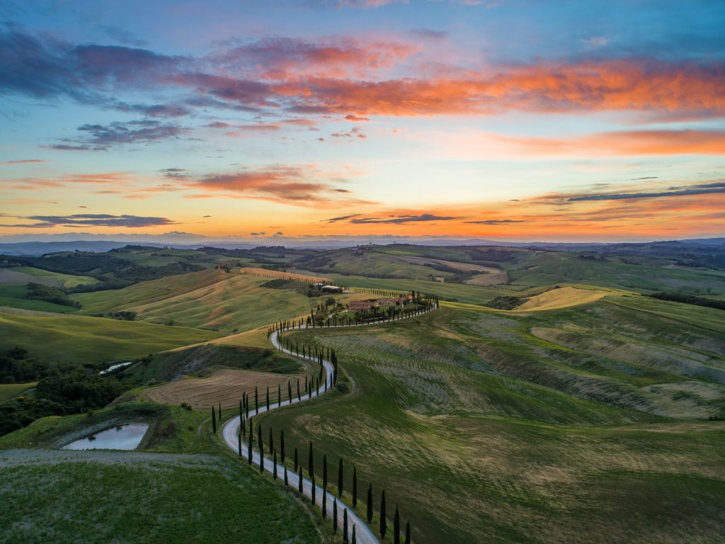 This image shows the rolling hills of Tuscany at sunset with a winding road.
