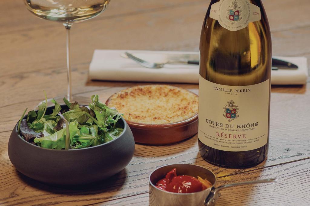 Famille Perrin's Cotes du Rhone Blanc on a table next to a salad and some cheese.
